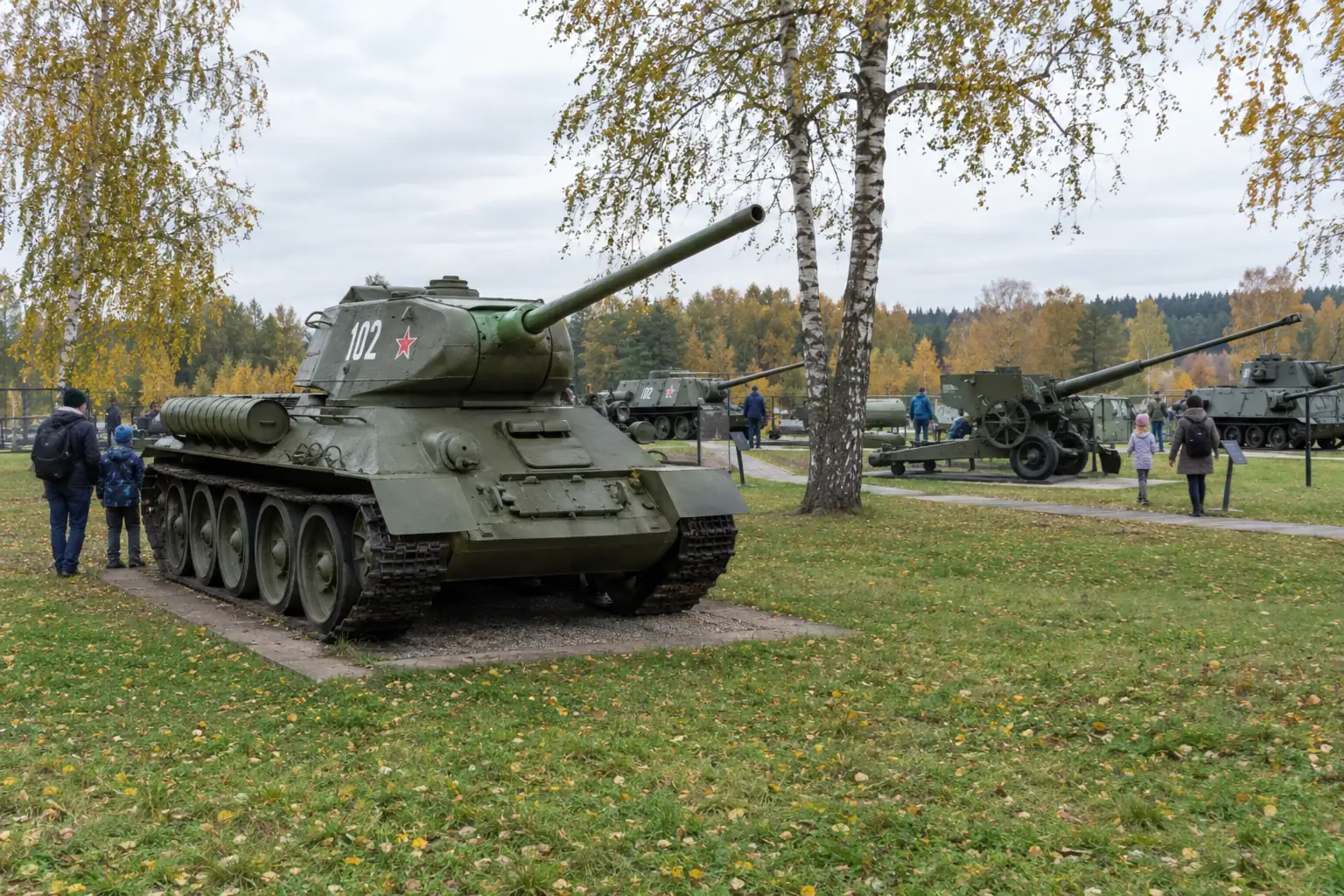 Xe tăng T-34 Xô Viết sơn xanh đặt trên bãi cỏ dưới hàng bạch dương mùa thu, khách tham quan đi quanh